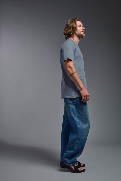 A male model wearing the unisex Organic Soft Cotton T-shirt in the color canyon blue, made from 100% certified organic cotton, shot from a full body side view. This shirt is unisex and made in the USA. #color_canyon-blue
