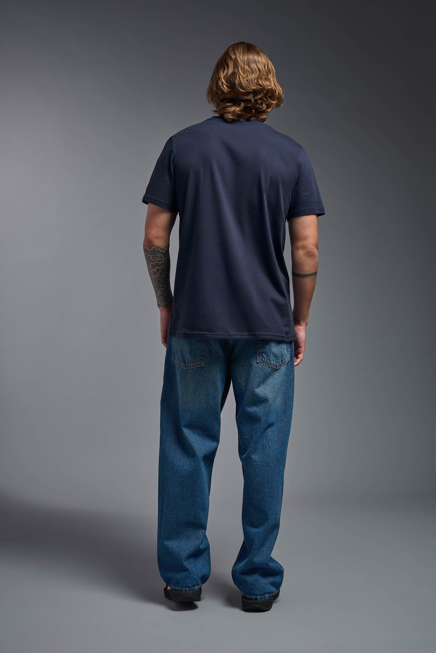 A male model wearing the unisex Organic Soft Cotton T-shirt in the color nova, made from 100% certified organic cotton, shot from a full body back view. This shirt is unisex and made in the USA. #color_nova