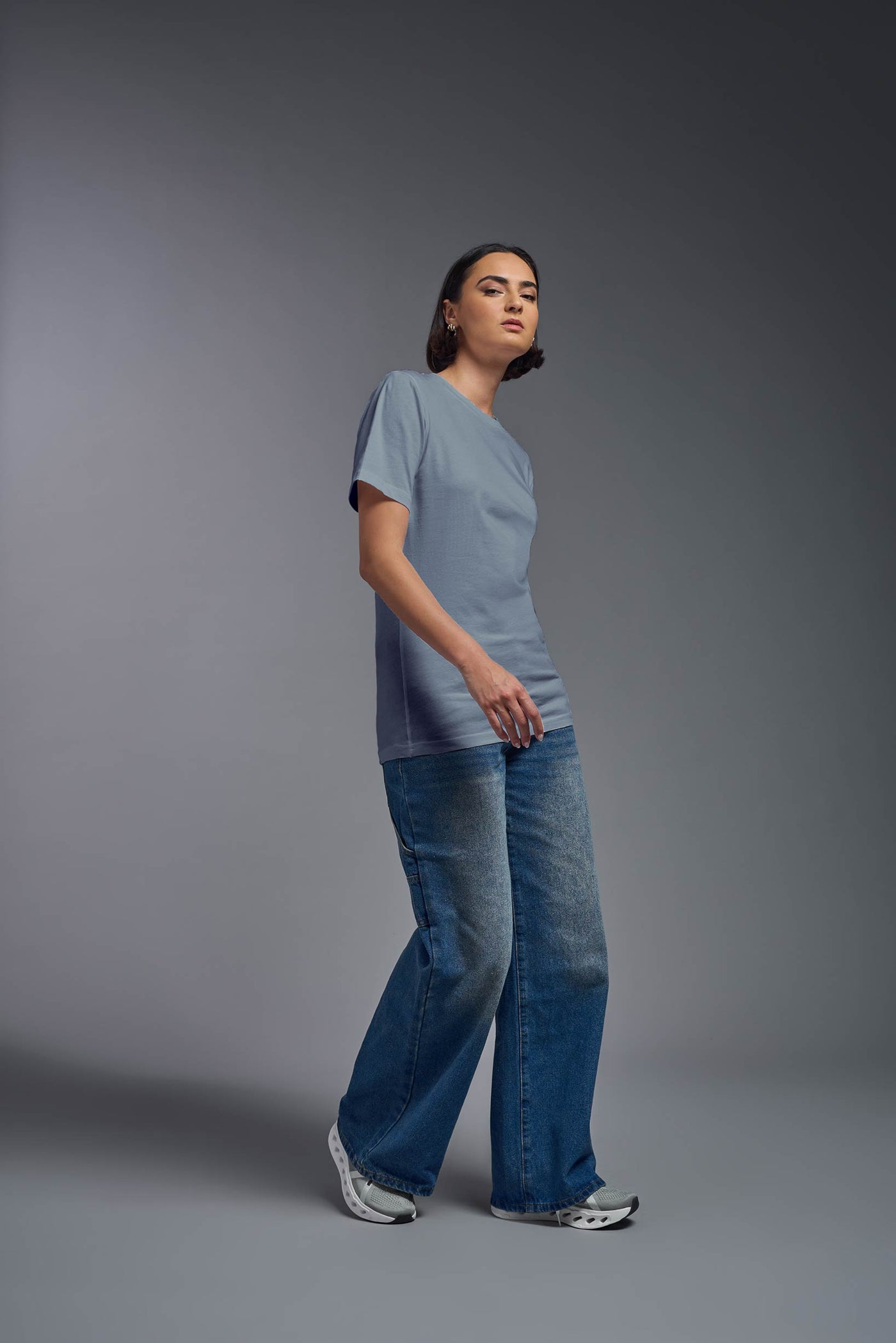 A female model wearing the unisex Organic Soft Cotton T-shirt in the color canyon blue, made from 100% certified organic cotton, shot from a full body side view. This shirt is unisex and made in the USA. #color_canyon-blue